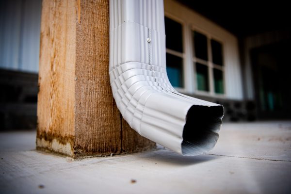 A closeup of a silver square labor hanging on a wooden pole with a house on a background
