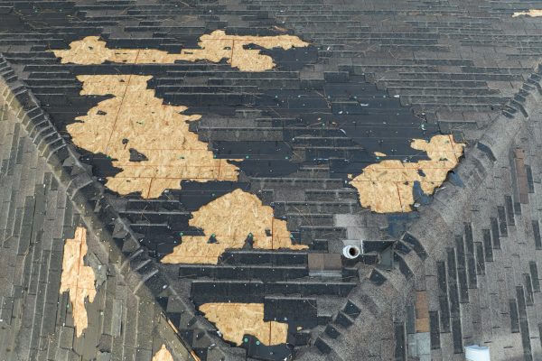 Ruined rooftop in need of repair. Wind damaged house roof with missing asphalt shingles after hurricane Ian in Florida.