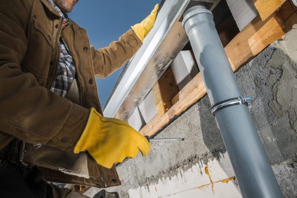 Construction Worker Finishing Installation of Eaves Roof Gutters. Industrial Theme.